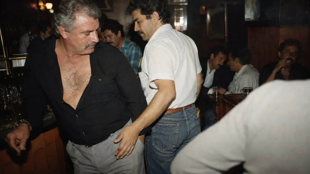 Recreación de hombres adultos que se rozan y observan en un bar gay de finales de los años ochenta o principios de los noventa.
