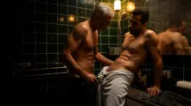 Dos hombres maduros comparten un momento de arreglo íntimo con una recortadora en un baño oscuro.