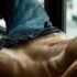 Torso de un hombre adulto recostado con los jeans abiertos y el pubis visible.