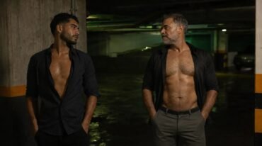 Un hombre joven adulto y un hombre maduro se miran con deseo en un estacionamiento nocturno.