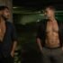 Un hombre joven adulto y un hombre maduro se miran con deseo en un estacionamiento nocturno.