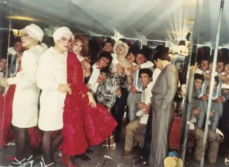 Grupo de personas con atuendos de fiesta y vestuario escénico frente a espejos en una fotografía de época.