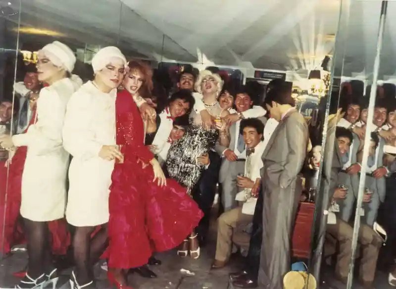 Grupo de personas con atuendos de fiesta y vestuario escénico frente a espejos en una fotografía de época.