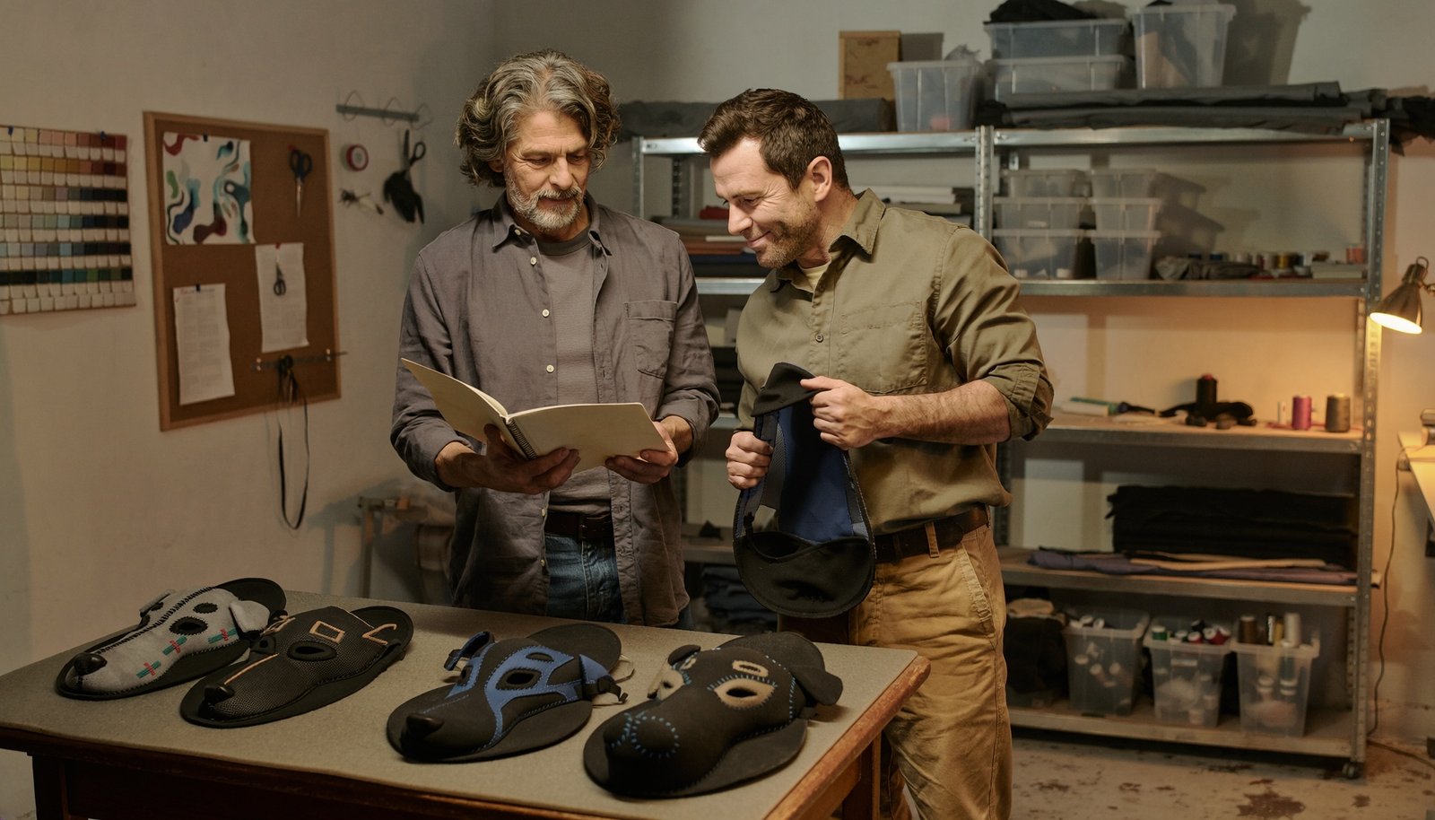 Dos hombres adultos conversan sobre máscaras y accesorios de juego canino dispuestos en una mesa de trabajo.