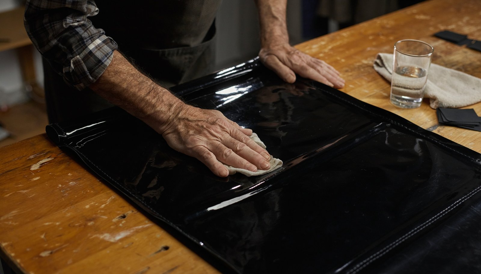Manos de un artesano adulto limpian cuidadosamente una pieza negra y brillante de material sintético sobre una mesa de taller.