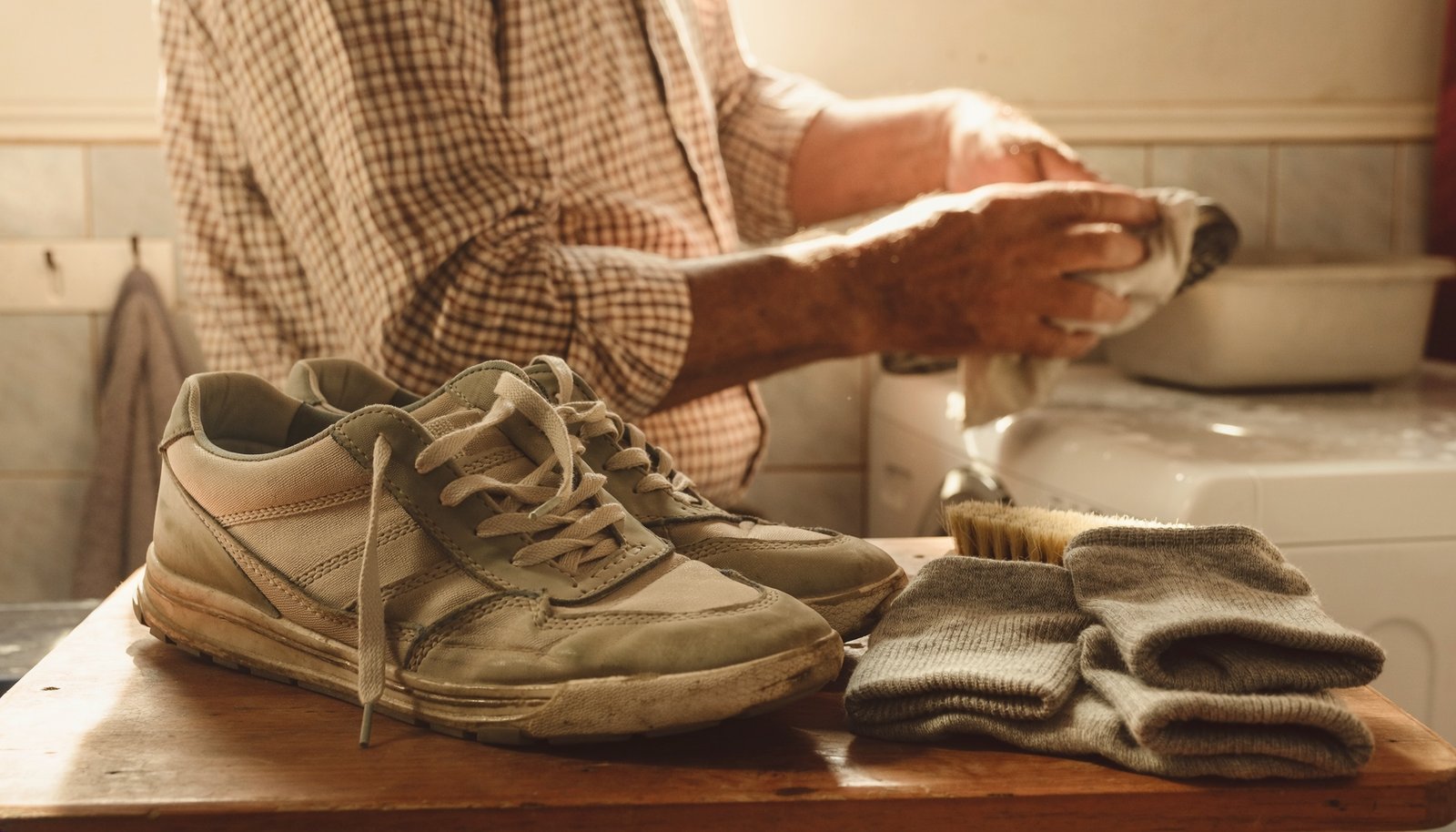 Tenis usados y calcetines grises doblados sobre una mesa mientras un hombre adulto limpia otra pieza de calzado.